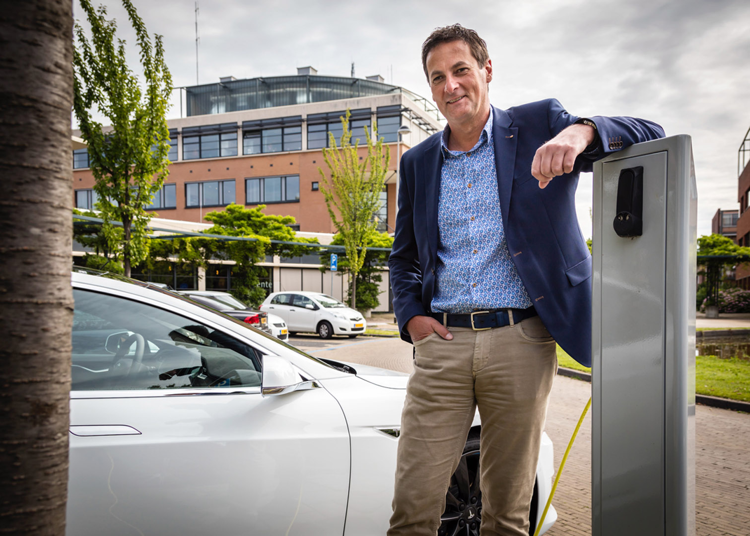 Een man naast een witte auto met een elektrische oplader.