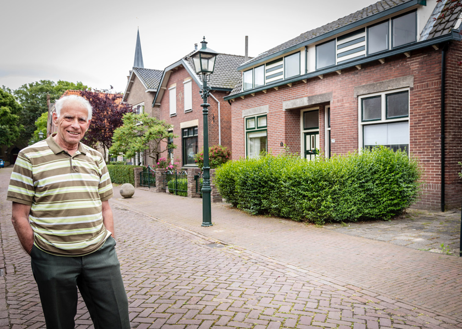 Een oude man staat op een stoep voor een huis.